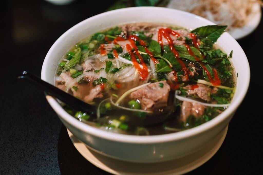 Delicious bowl of traditional Vietnamese pho garnished with fresh herbs and spicy sauce.
